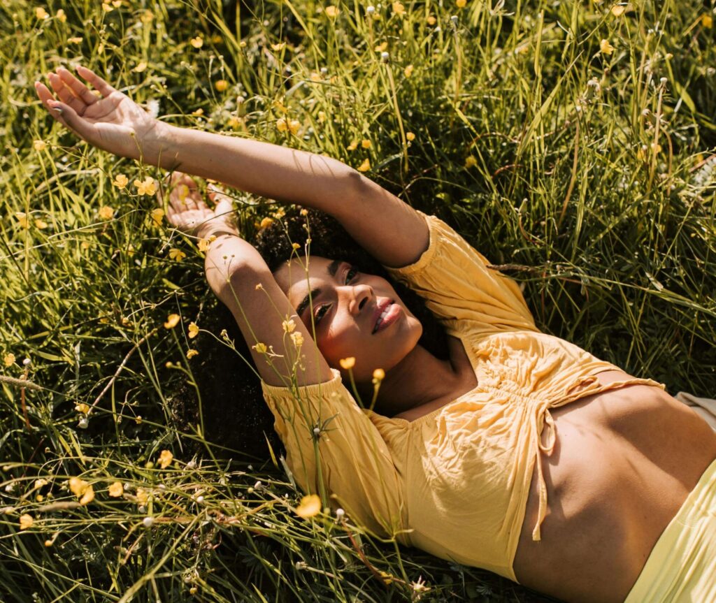 Black woman lying on the grass, eyes closed, looking peaceful and grounded, symbolising relief from anxiety.