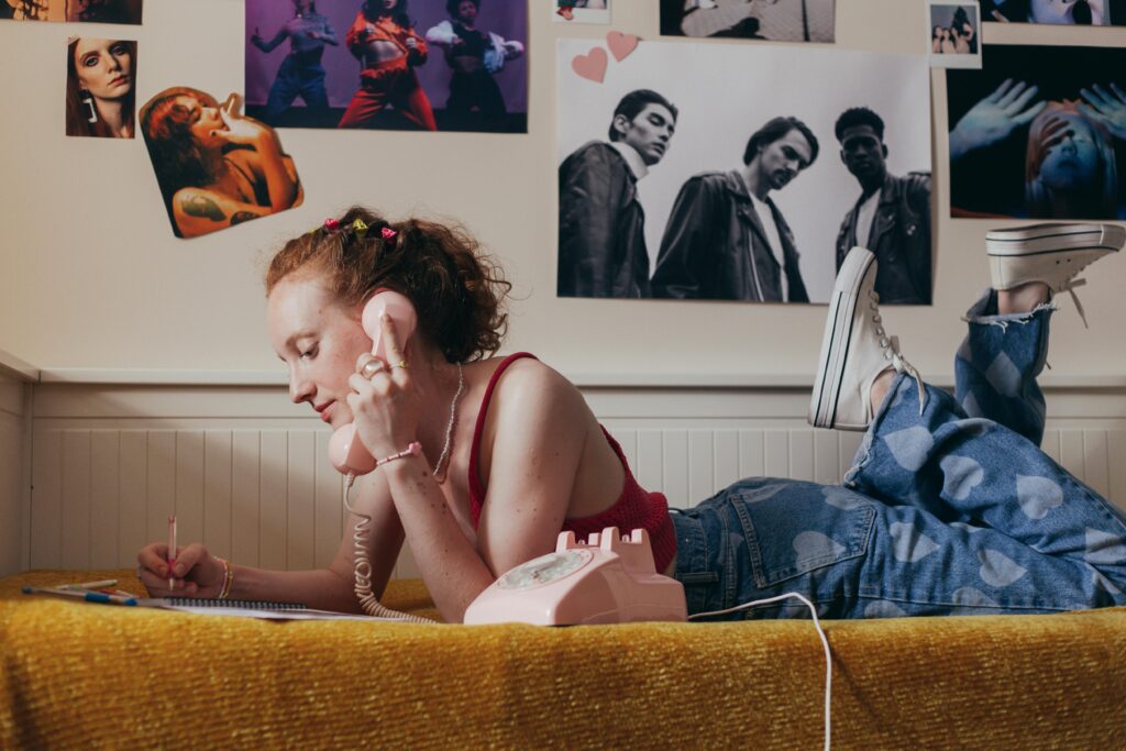 Young woman writing in diary while talking on a vintage phone indoors.