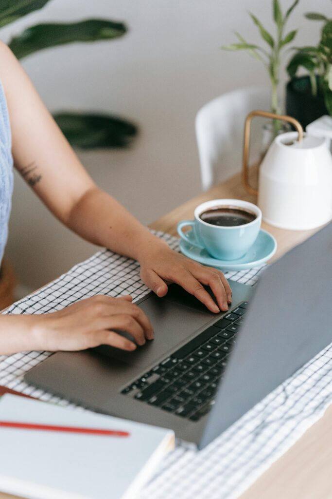 A woman typing on a laptop at a table with a cup of coffee, creating a cozy workspace vibe.