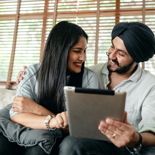 A joyful couple using a tablet indoors, embracing and smiling together.